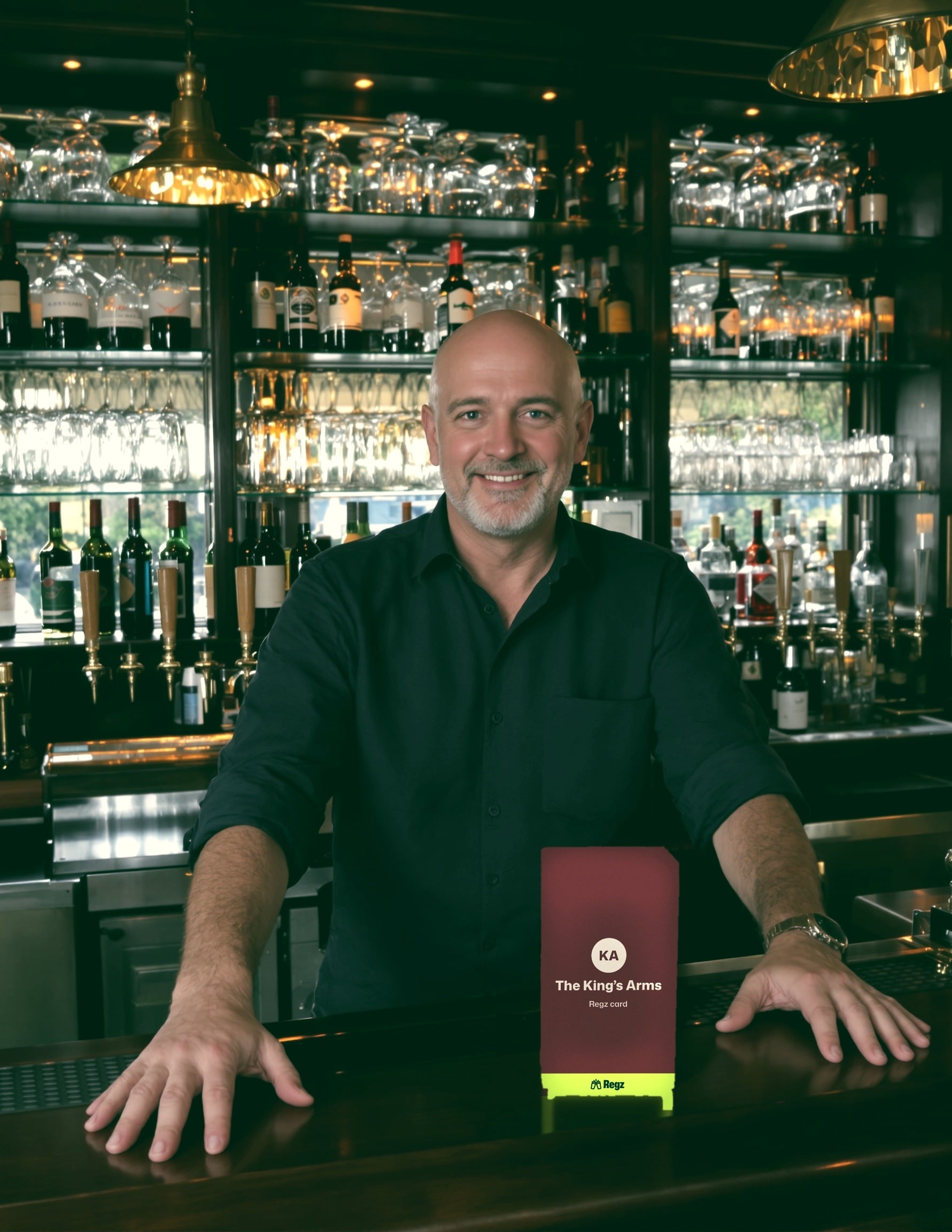A smiling landlord behind his bar, with a sign for The King's Arms Regz card on the counter